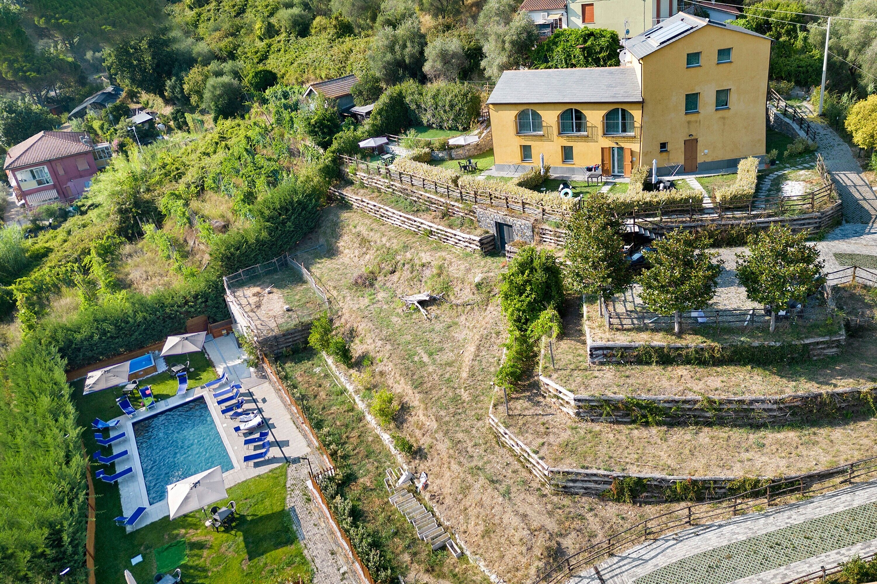 An aerial view of a residential area with a swimming pool, a yellow building, and surrounding greenery.