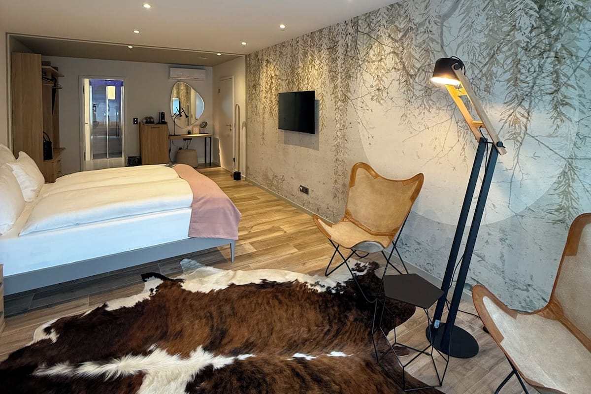 Une chambre à coucher moderne, dotée d’un lit, d’un grand miroir, d’un téléviseur à écran plat et d’une fresque murale originale.