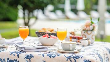 A breakfast table with a floral tablecloth, two glasses of orange juice, a bowl of fruit, and a cup of coffee.