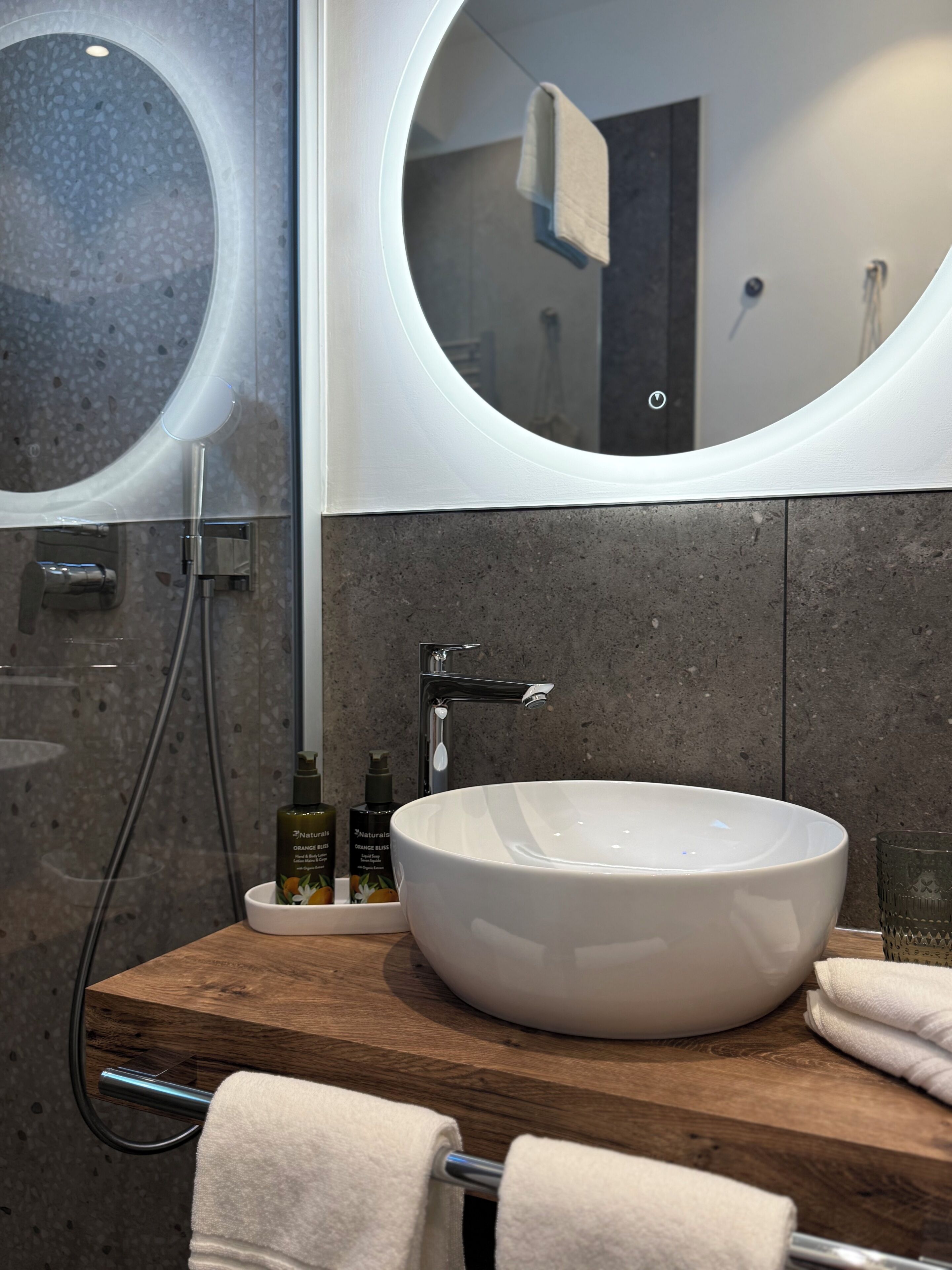 A bathroom with a round mirror, a white sink, and a wooden countertop.