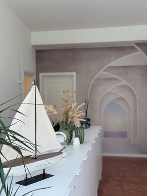Un intérieur moderne avec une maquette de voilier posée sur un comptoir blanc, une porte et un couloir doté d’un plafond en arc de cercle.