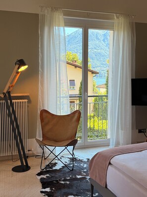 A room with a bed, a chair, a radiator, a lamp, and a view of a mountain through a window. -  LA VILLA, a Swiss Quality Hotel (Minusio)