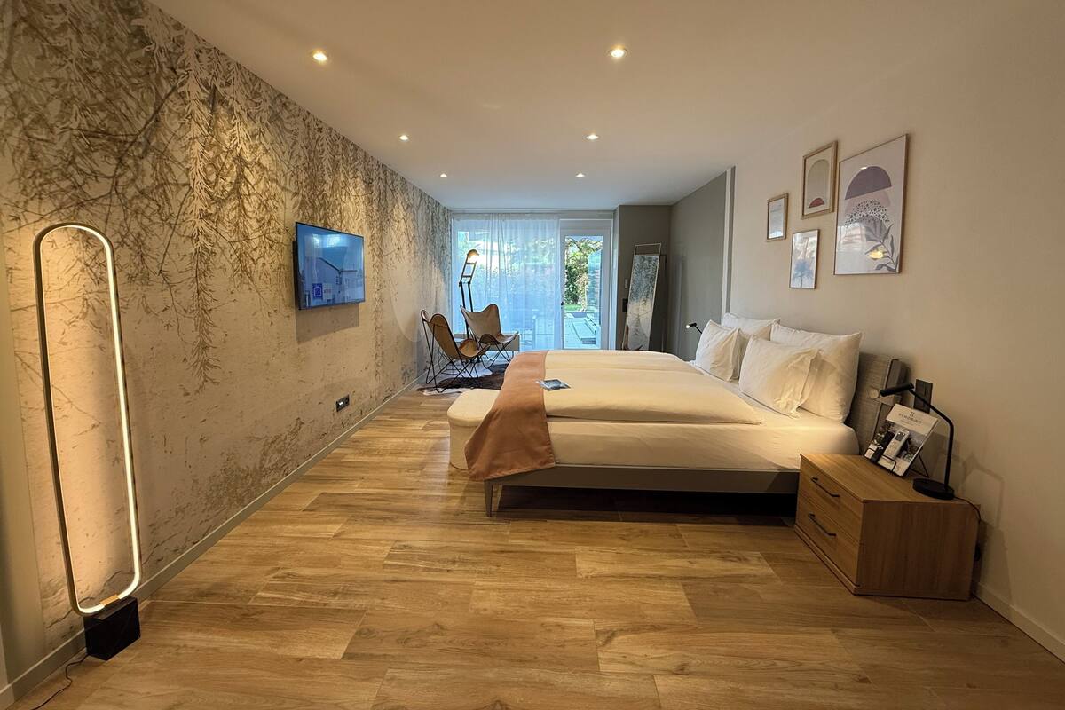 Une chambre à coucher moderne avec un grand lit, un téléviseur fixé au mur et un plancher en bois.