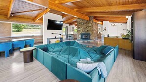 Un salón amplio con un sofá modular grande color turquesa, vigas de madera en el techo, una chimenea de piedra y un televisor de pantalla plana montado en la pared.