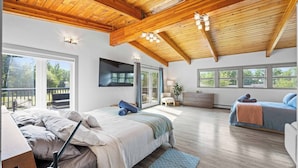 Un dormitorio amplio con una cama grande, un escritorio y una cama adicional. Cuenta con varias ventanas y un balcón.