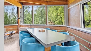 Un comedor moderno con techo de madera, ventanas amplias y sillas azules alrededor de una mesa central.