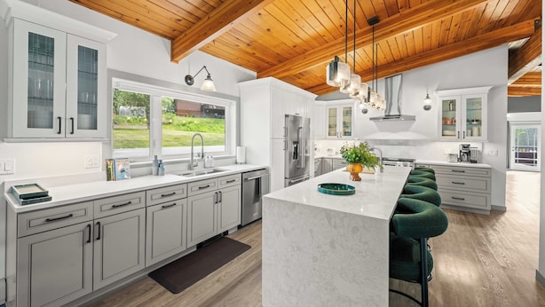 Una cocina moderna con armarios blancos, una isla grande y vigas de techo de madera.