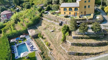 An aerial view of a residential area with a swimming pool, a yellow building, and surrounding greenery.