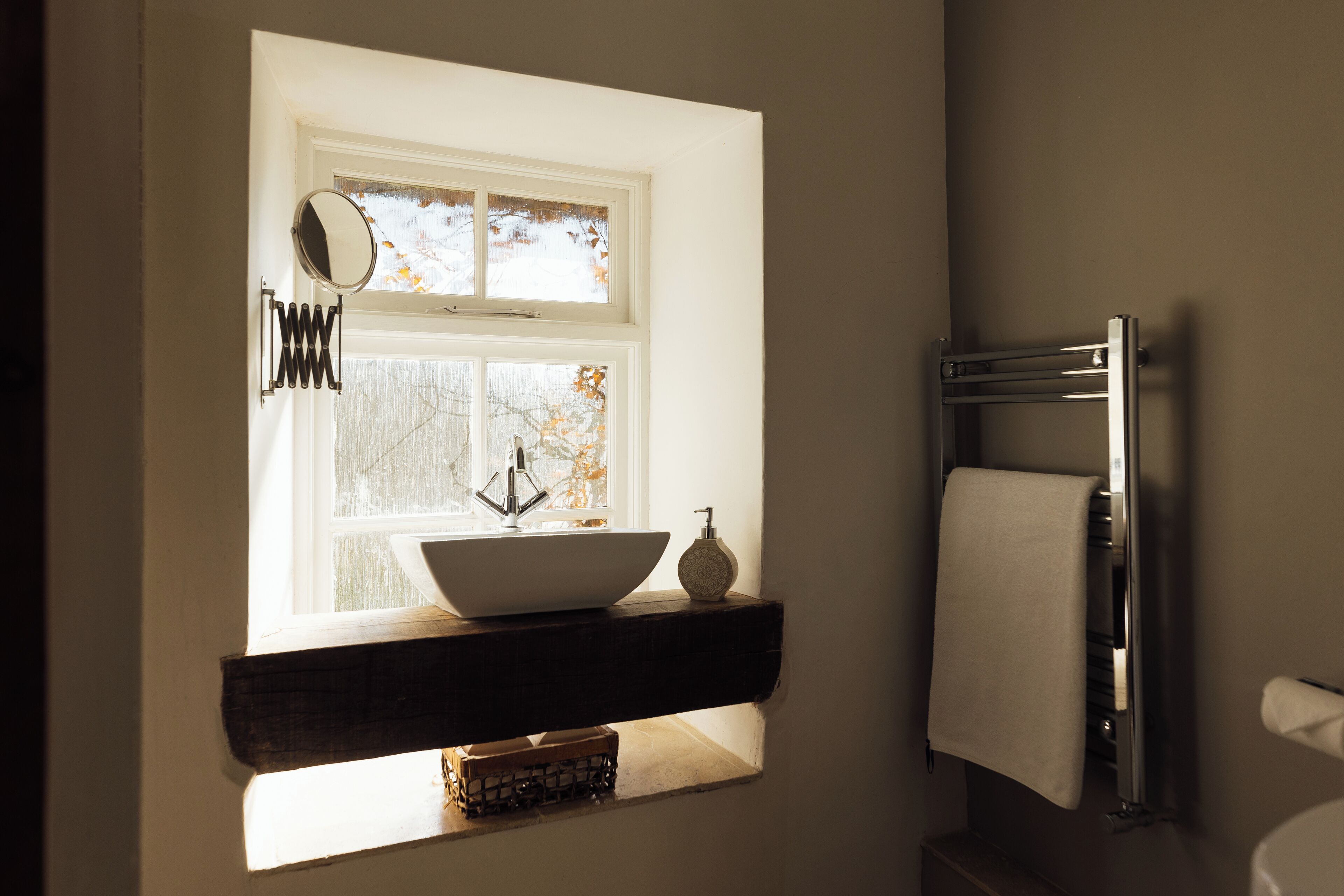 A bathroom with a window, a sink, a towel rack, and a mirror.