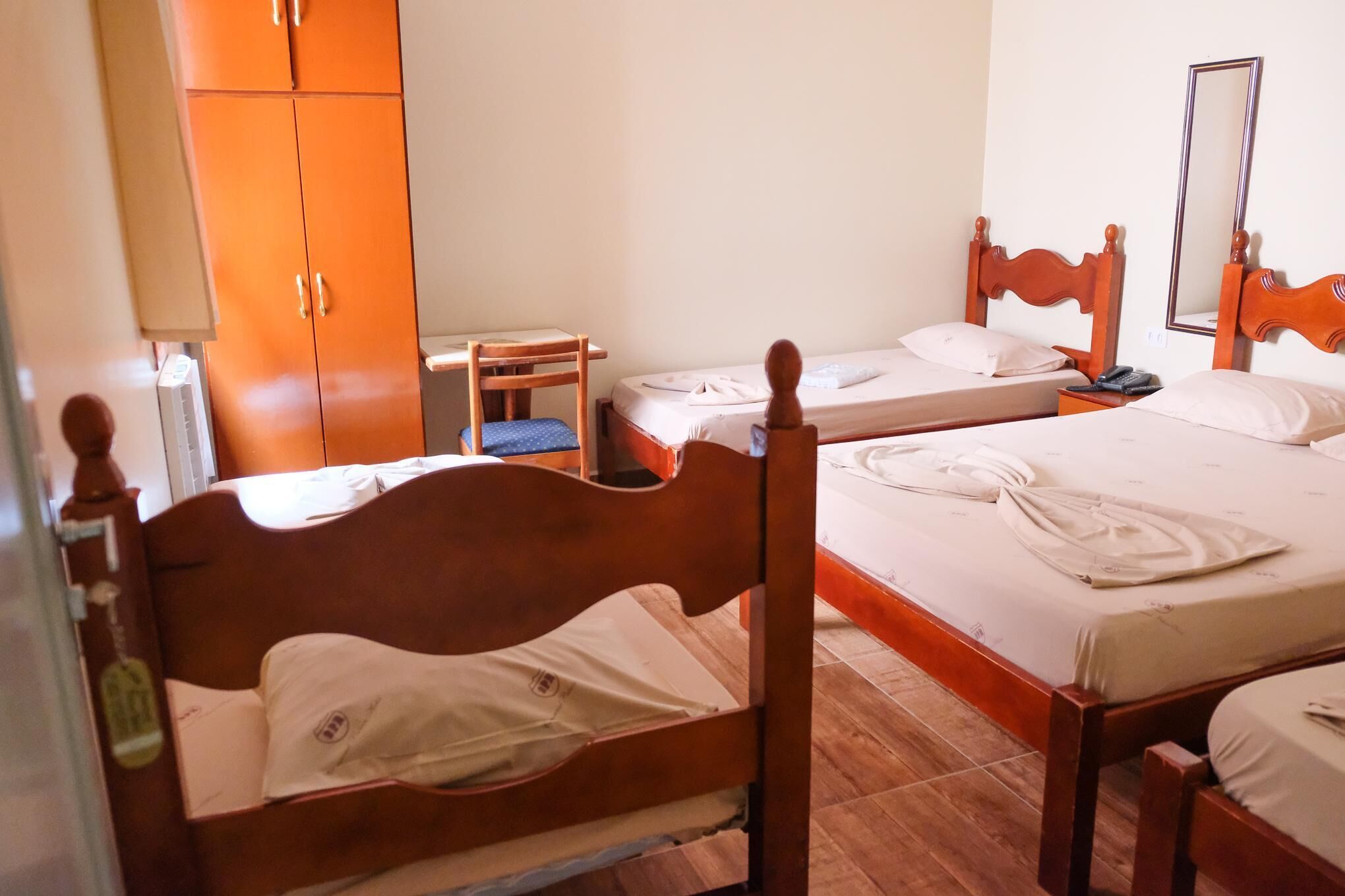 A hotel room with two single beds, a wooden wardrobe, a desk, and a chair.
