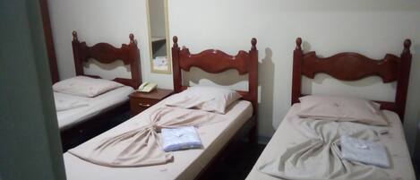 A hotel room with two single beds, wooden headboards, a bedside table with a lamp, and a mirror on the wall.
