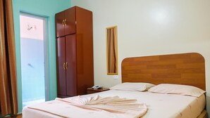 Un dormitorio con cabecera de madera, una cama con una colcha rosa ordenada, un armario y una mesita de noche con un teléfono.
