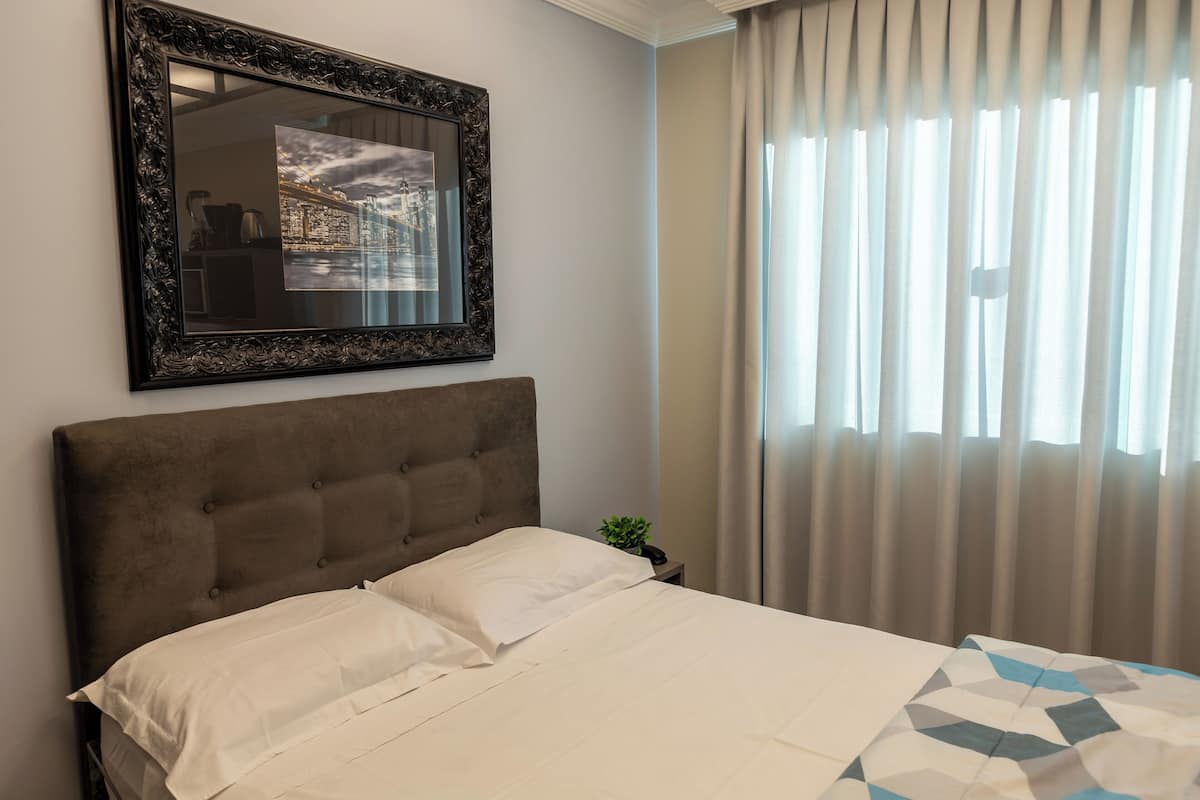 A neatly made bed with a headboard, a framed picture on the wall, and a window with curtains.