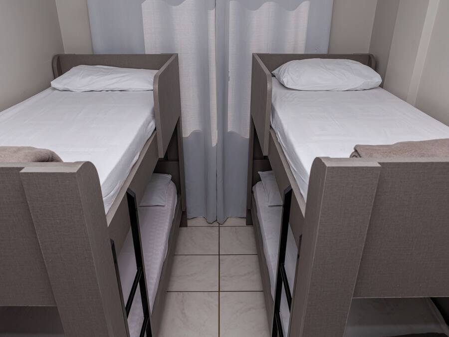 Duas camas de solteiro com lençóis brancos, um divisor de cortina e um piso ladrilhado.