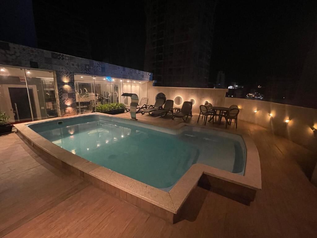 A rooftop swimming pool with lounge chairs and a glass-enclosed building in the background.