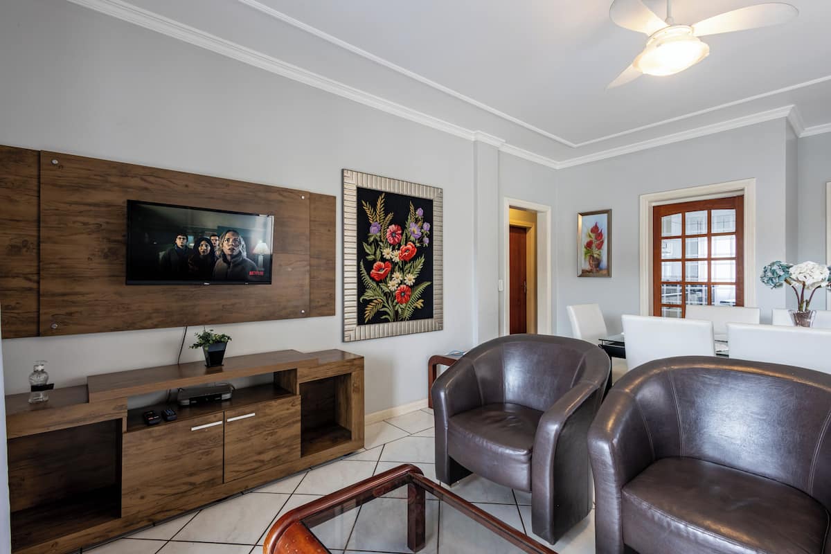 A living room with a flat-screen TV, wooden entertainment unit, leather chairs, and a ceiling fan.