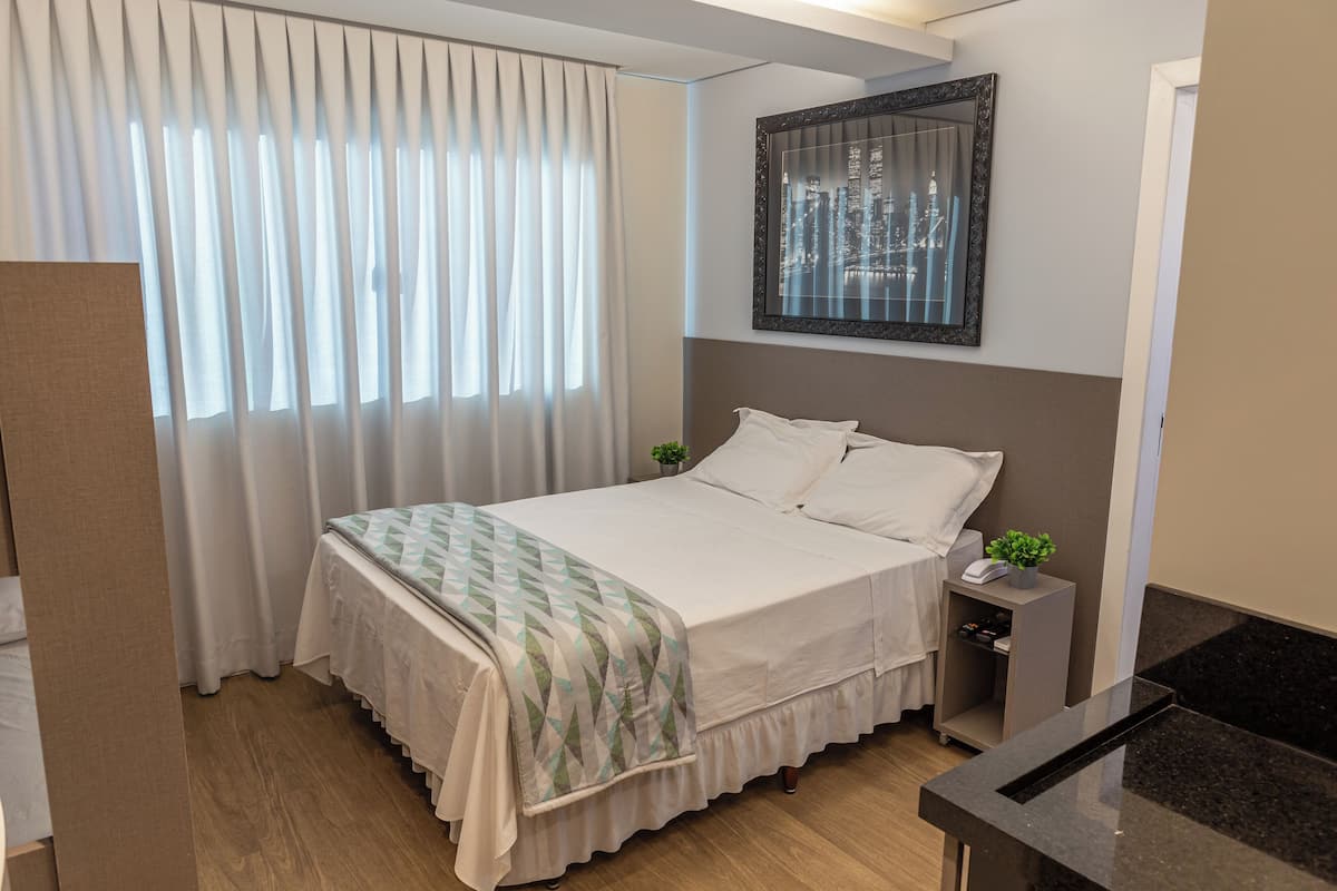 A neatly arranged hotel room with a bed, bedside table, and a view of a cityscape through the window.