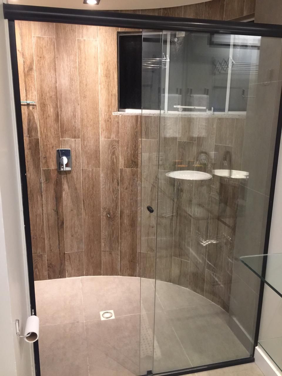 A modern shower enclosure with wooden paneling and glass doors, featuring a toilet paper holder and a visible shower control panel.