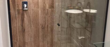A modern shower enclosure with wooden paneling and glass doors, featuring a toilet paper holder and a visible shower control panel.