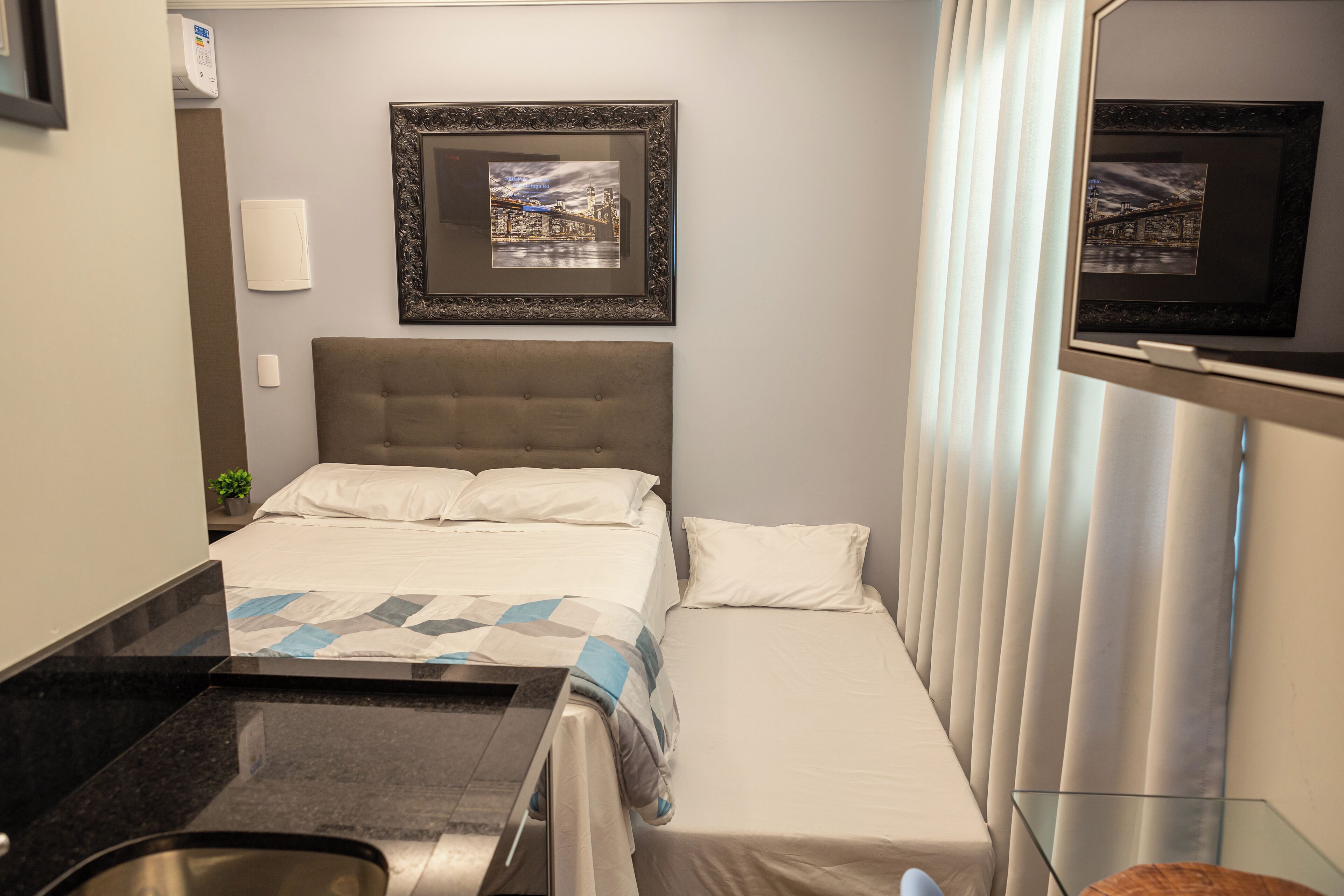 A hotel room with a bed, a small desk, a mirror, and a framed picture on the wall.