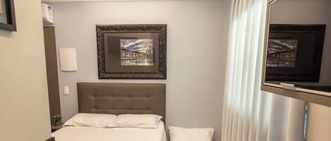 A hotel room with a bed, a small desk, a mirror, and a framed picture on the wall.