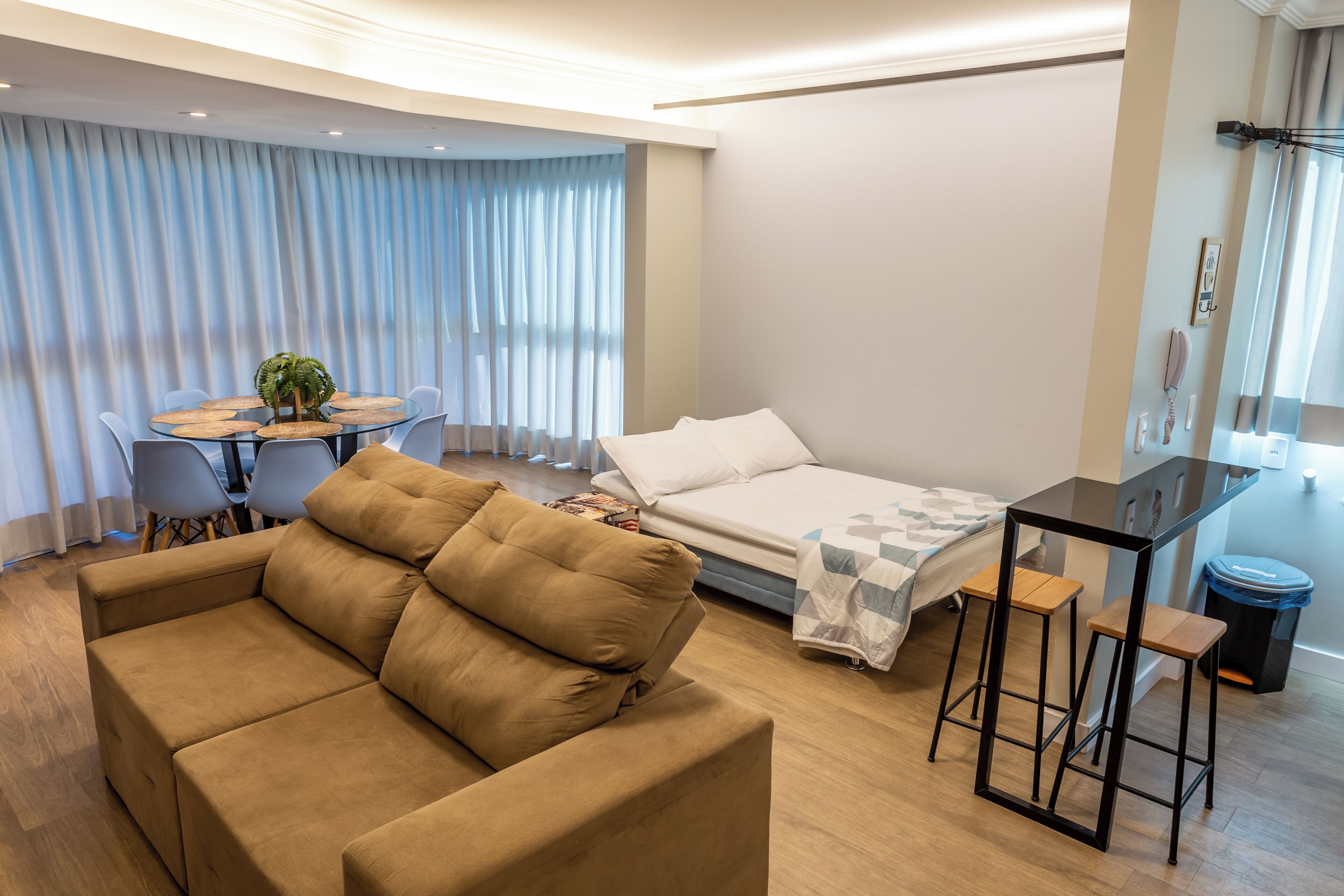 Una habitación de hotel moderna con sofá, cama, mesa de comedor y una pequeña cocina.