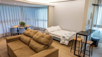 Una habitación de hotel moderna con sofá, cama, mesa de comedor y una pequeña cocina.