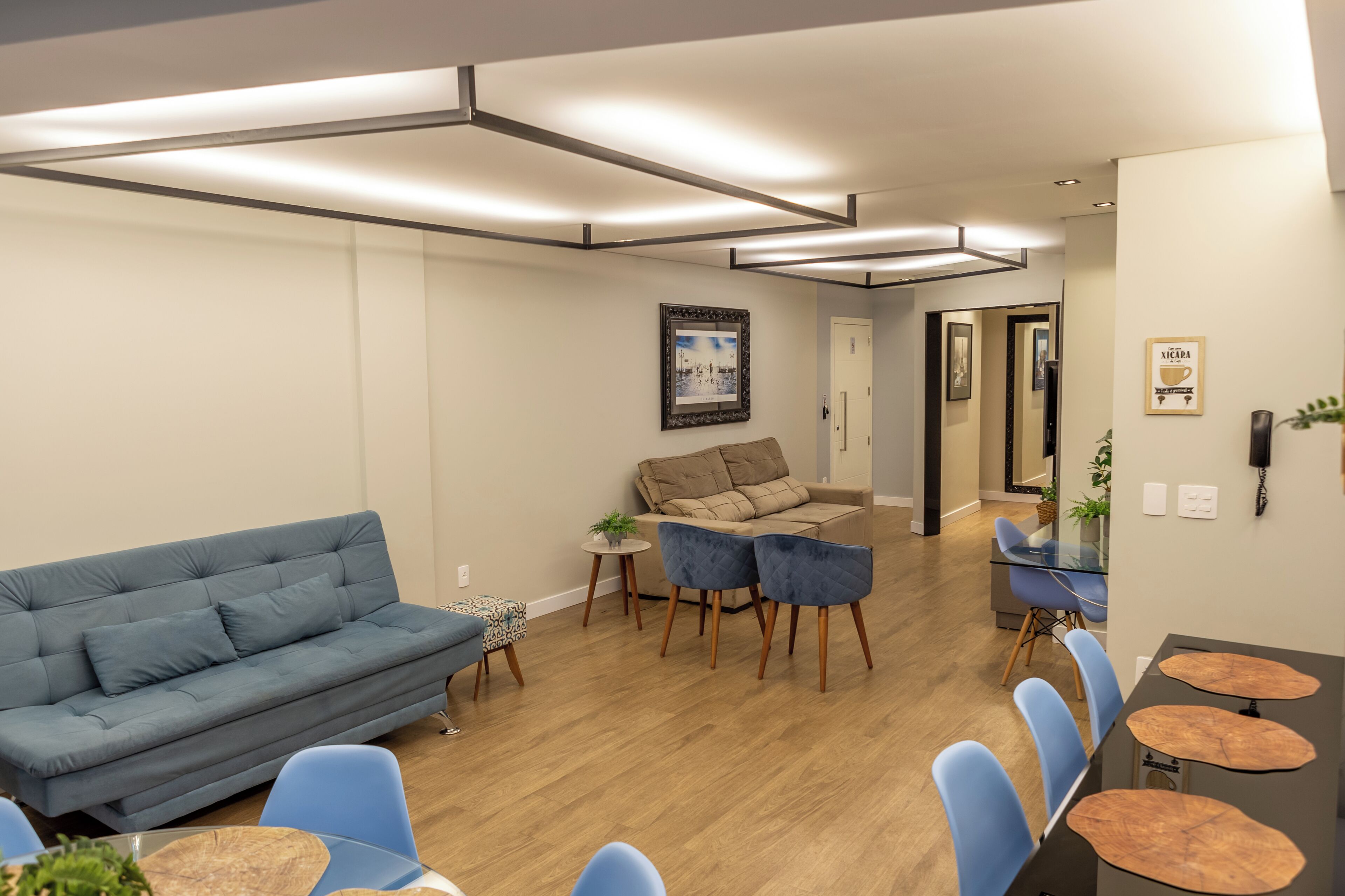 A modern living room with a blue sofa, a beige sofa, and a glass dining table with blue chairs.