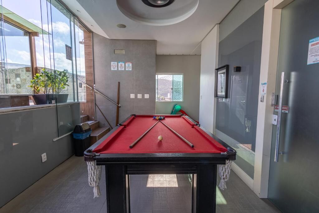Une table de billard dans une pièce dotée de grandes fenêtres, d’une poubelle et d’une porte portant un panneau indiquant la sortie de secours.