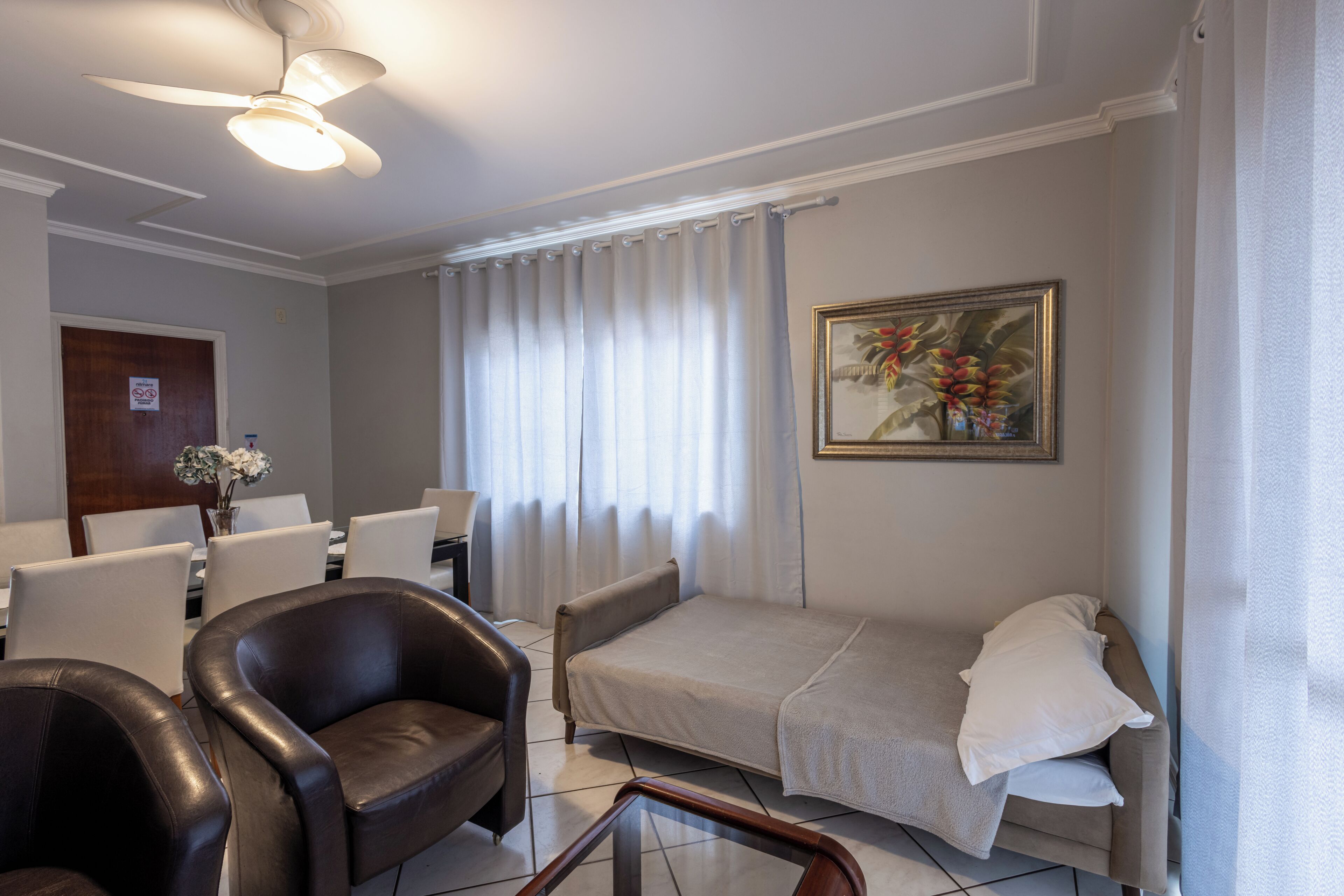 A hotel room with a bed, a desk, a chair, a ceiling fan, and a painting on the wall.