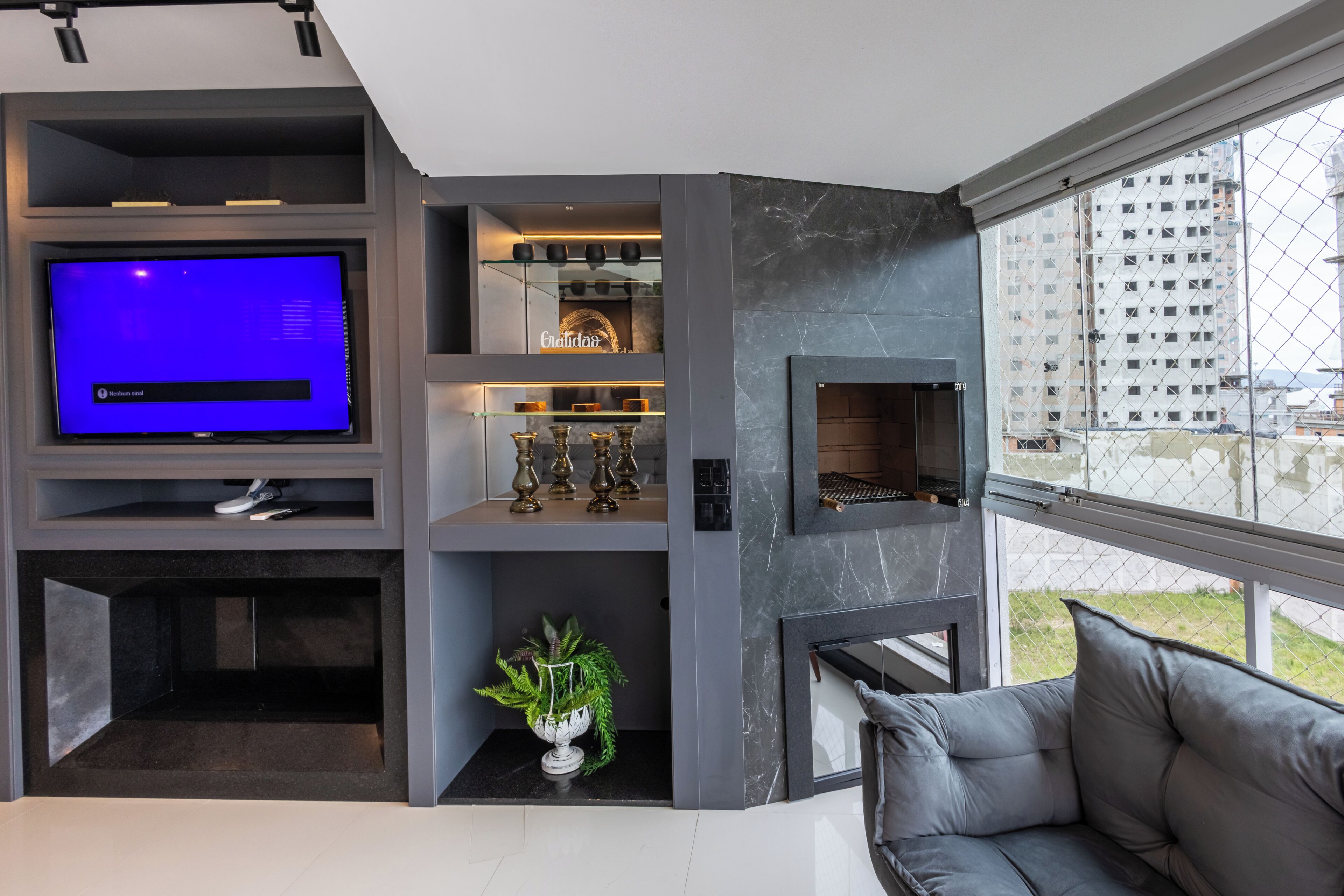 A modern living room with a flat-screen TV, built-in shelves, a fireplace, and a large window with a city view.