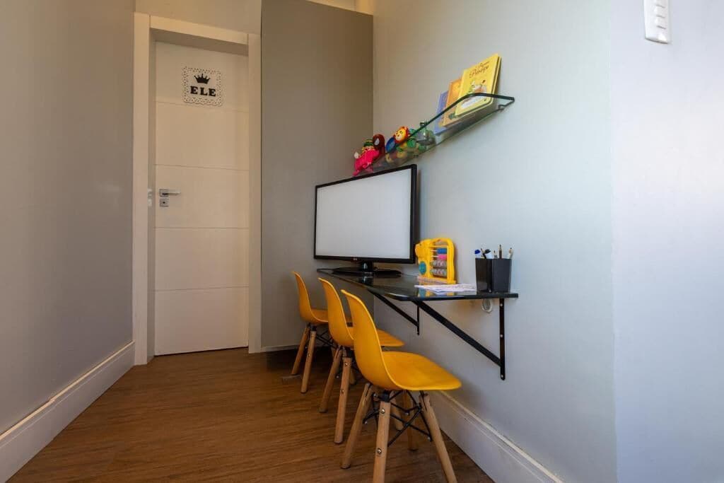 A small room with a white door, a computer on a desk, and three yellow chairs.