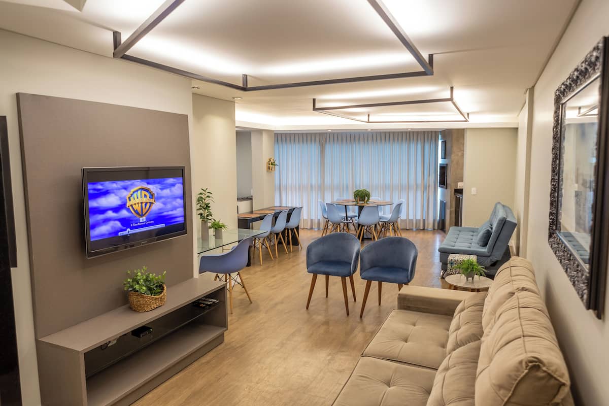 A modern living room with a flat-screen TV, a sofa, and a dining area with chairs and a table.