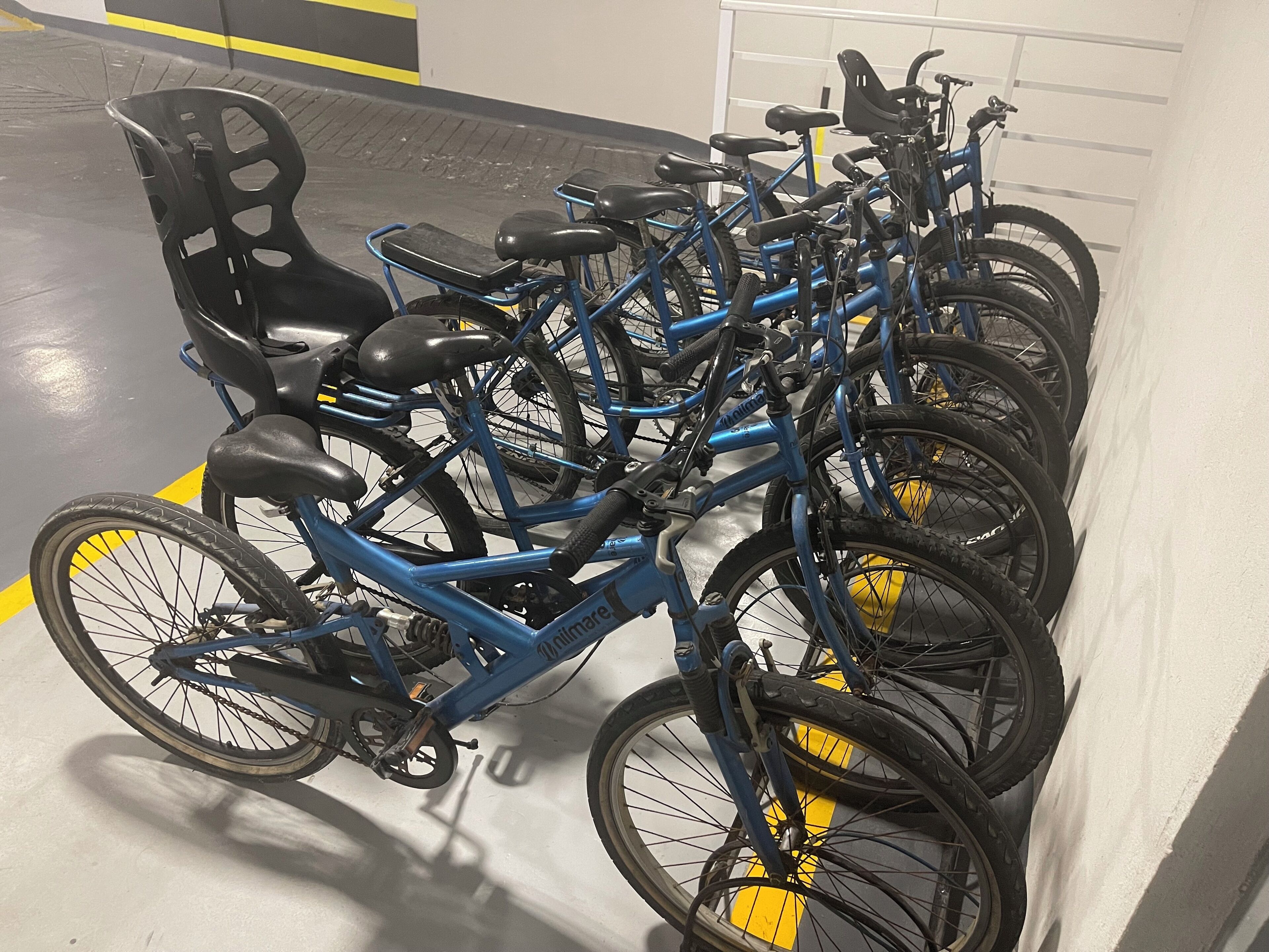 A row of blue bicycles parked in a designated area with yellow lines on the floor.