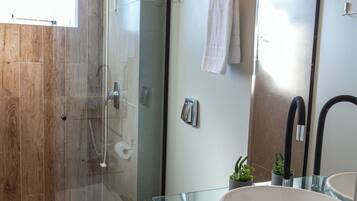 Un baño moderno con cabina de ducha de vidrio, inodoro blanco, lavabo de vidrio y un espejo grande.
