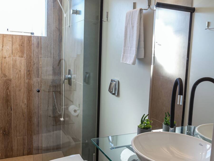 Un baño moderno con cabina de ducha de vidrio, inodoro blanco, lavabo de vidrio y un espejo grande.