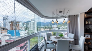 A modern apartment with a balcony, a dining area, and a view of the cityscape. - Nilmare Apart Hotel (Itapema)