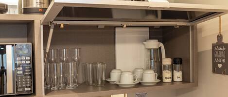 A kitchen with a coffee maker, kettle, blender, and various glassware.