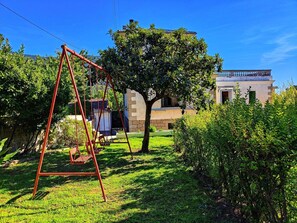 A garden with a swing set, a tree, and a building with a balcony. - Large Holiday Home 'El Rozado' for 22 Guests with Garden in Sierra de Gredos (Piedralaves)