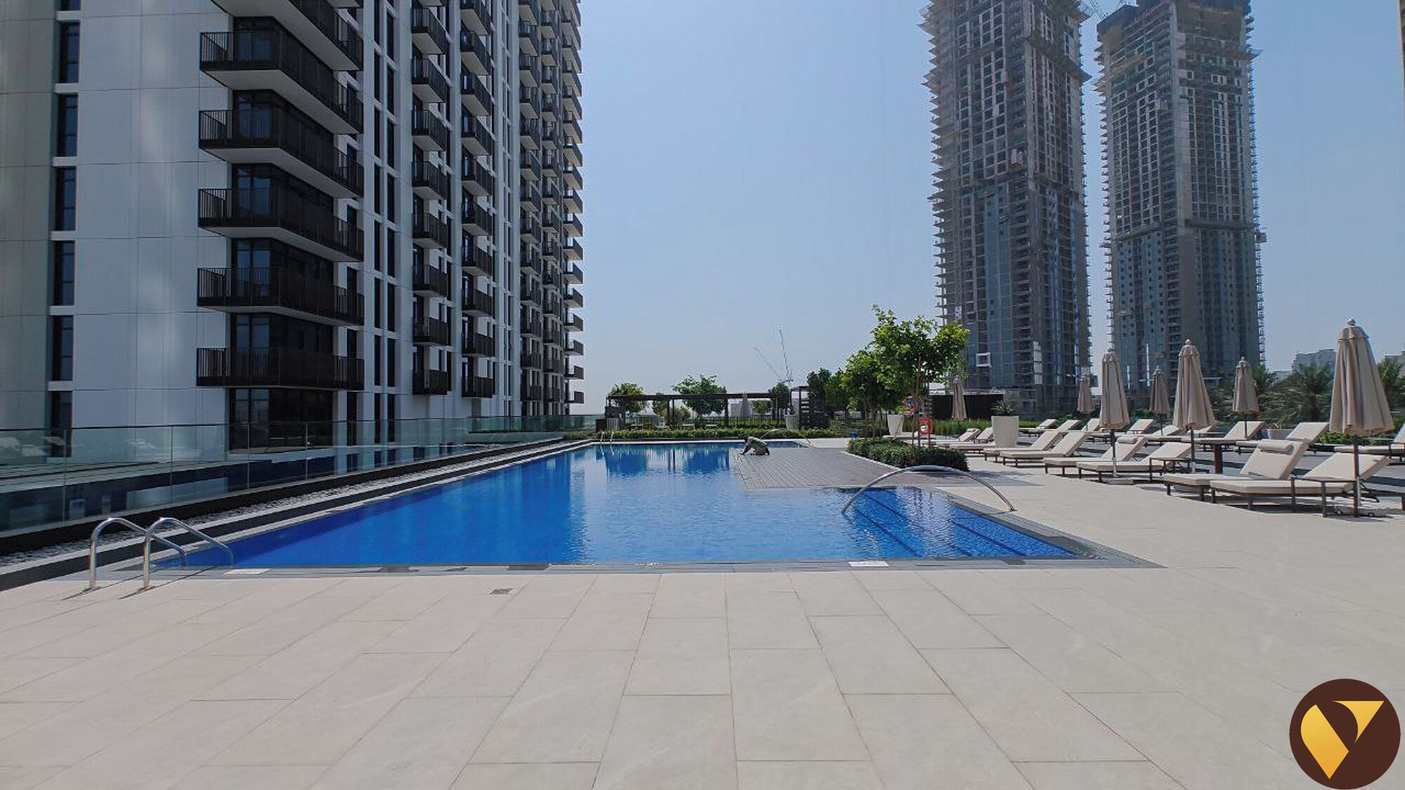 A swimming pool area with lounge chairs and umbrellas, surrounded by high-rise buildings.
