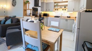 A compact kitchen with modern appliances, a dining area with a wooden table, and a living space with a sofa and decorative pillows. - Rainbow's End (Dereham)
