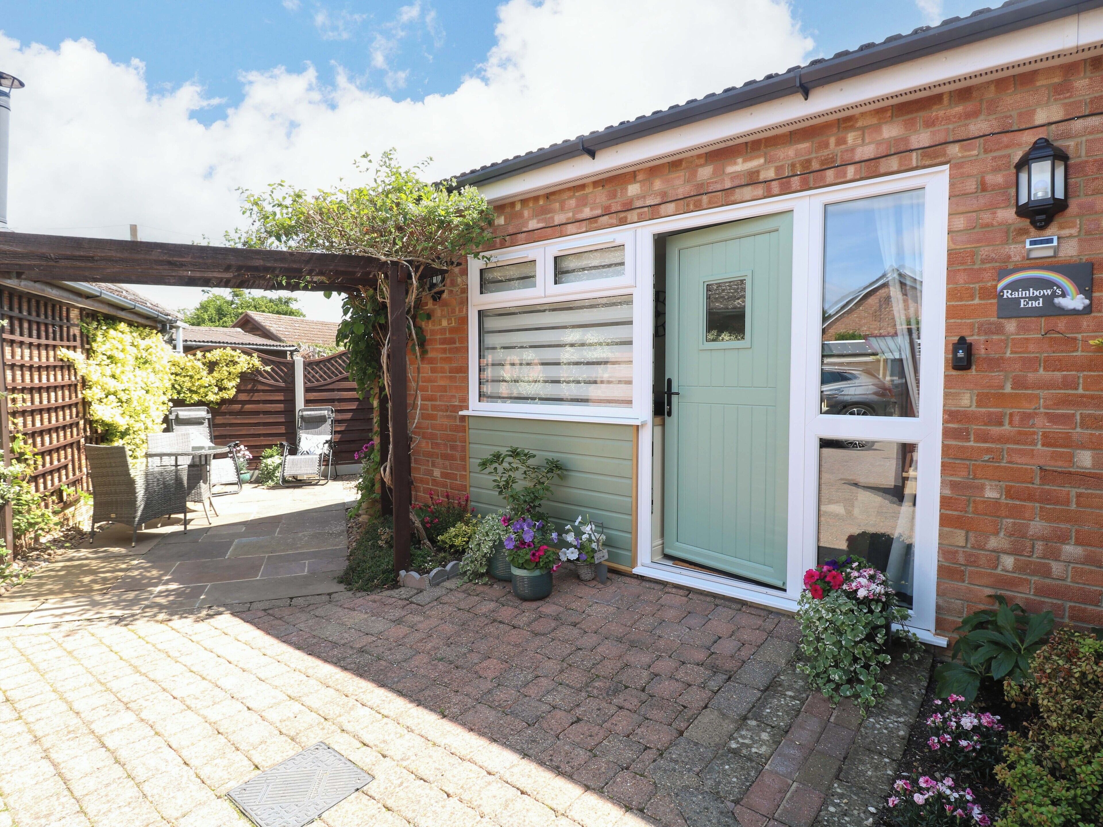 A brick house with a green door, a garden with flowers, and a sign that says "Rainbow's End".