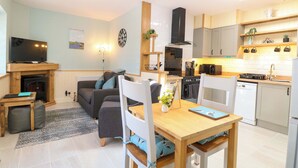 A modern living room with a fireplace, sofa, and TV. The kitchen has white cabinets, a stove, and a microwave. - Rainbow's End (Dereham)