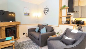 A cozy living room with a fireplace, a television, a sofa, and a dining area with a microwave. - Rainbow's End (Dereham)