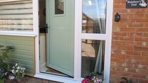 A light green door with a small window and a welcome mat. There is a brick wall with a sign that says "Rainbow's End". - Rainbow's End (Dereham)