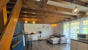 Una cocina moderna con techo de madera, zona de comedor con taburetes, sofá y microondas en la encimera.