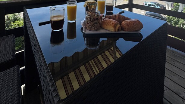 Una mesa con alimentos y bebidas para el desayuno en un balcón con vistas a un paisaje verde y casas.