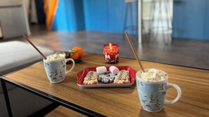Una mesa de madera con dos tazas, una bandeja de pasteles y una vela encendida en una cocina moderna con armarios azules.