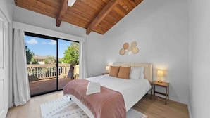 A bedroom with a large bed, a nightstand, a lamp, and a view of the outside.