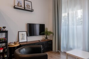 Un salón con televisor de pantalla plana, un mueble de madera, un sofá de cuero negro y una planta en maceta.